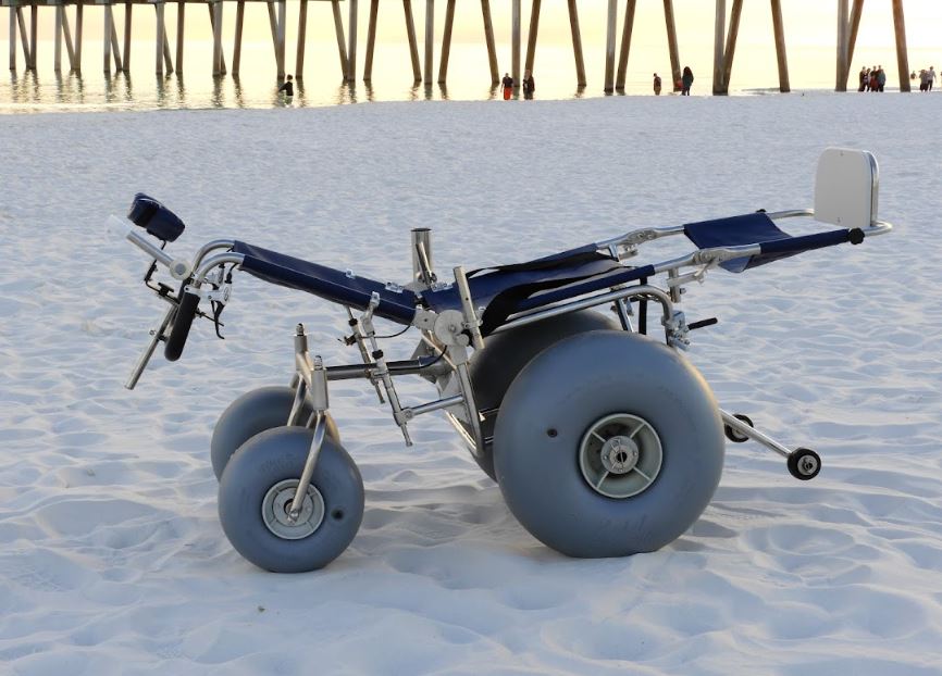 reclining wheelchair reclined with the legs out with no passenger on the beach in the sand.