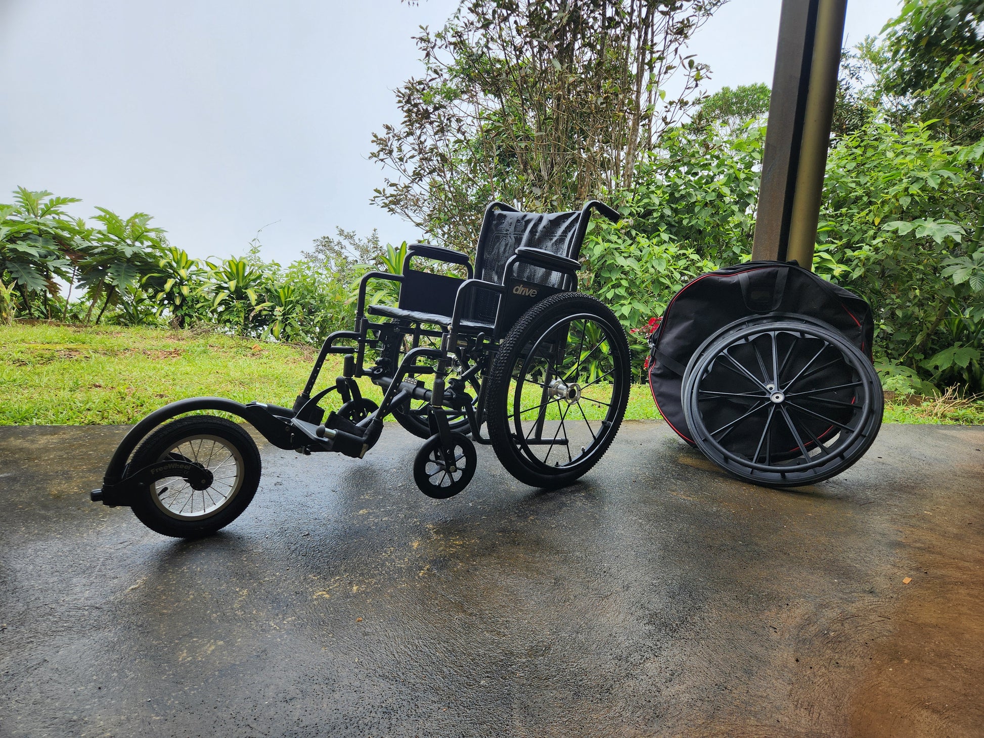 Three-wheeled wheelchair on a wet pavement with greenery in the background