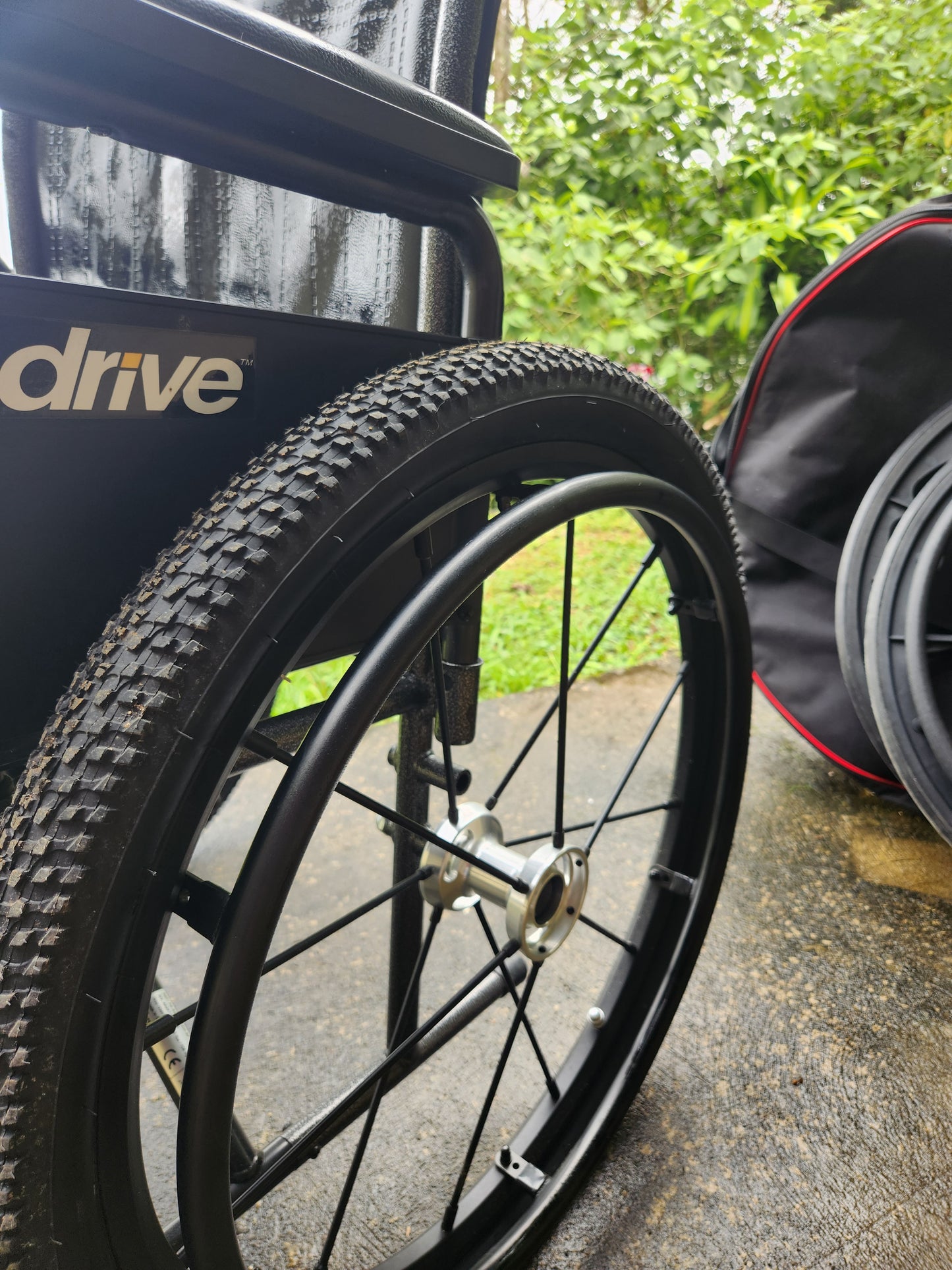 Close-up of a wheelchair wheel with a visible Drive Medical brand logo on a blurred outdoor background