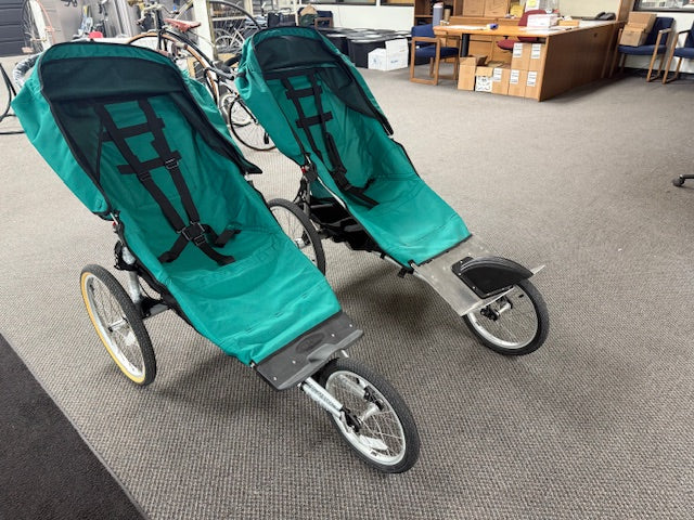 Two teal strollers on a gray floor in an indoor setting